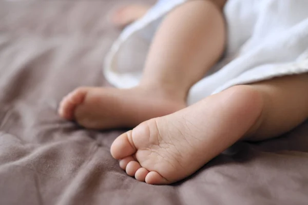 Pés de bebê tirando uma soneca com lençóis castanhos — Fotografia de Stock