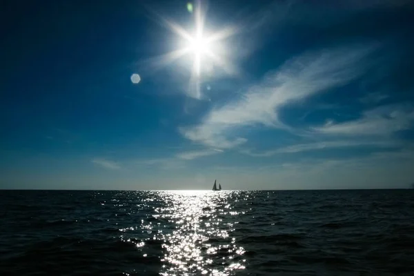 В море плывет одинокая парусная лодка и солнце в драматическом небе — стоковое фото