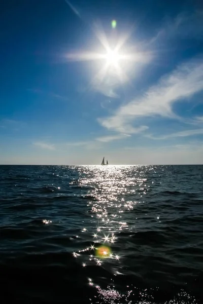 В море плывет одинокая парусная лодка и солнце в драматическом небе — стоковое фото