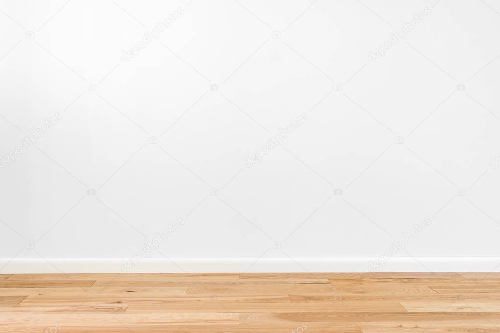 White painted stucco wall and natural wooden ash-tree 3-band parquet board hardwood floor. Flooring in scandinavian style of empty interior with wide white baseboards. Light brown, biscuit color