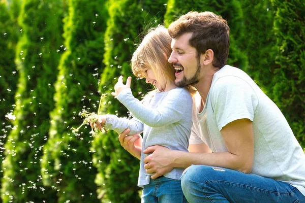 Joyeux père et fille rient et jouent avec des fleurs de pissenlit Image En Vente