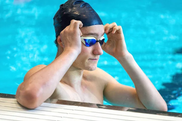 Um atleta adolescente melhora os óculos de natação em uma piscina interior. C — Fotografia de Stock
