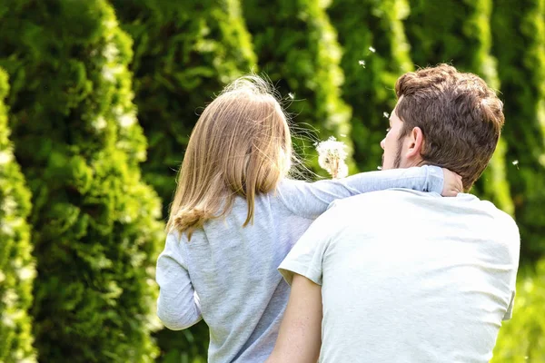 Back view. Father and daughter blowing dandelion flowers. — Stock Photo, Image