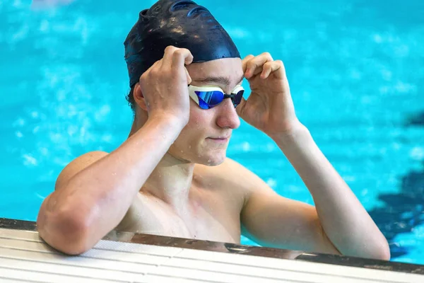 Un sportiv adolescent îmbunătățește ochelarii de înot într-o piscină interioară. C Fotografie de stoc