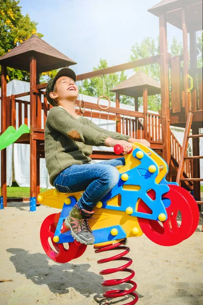 Niña feliz montar en motocicleta en el patio de recreo solo en tiempo soleado —  Fotos de Stock