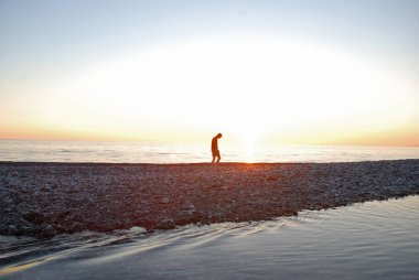 Genç bir adam yalnız nehir kıyısında ve deniz arasında yürüyor