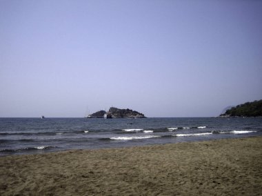 Sakin ve güneşli bir havada kumsal. Zayıf dalgalar kıyıdaki kumları okşuyor..