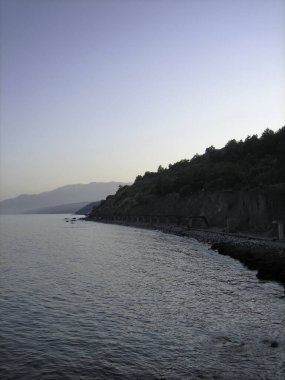 Gün batımında Rocky Coast. Uzakta, kıyı dağları sisin içinde belirdi..