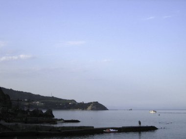 Sakin bir denizin kıyısındaki dalgalı su... kıyı dağlarının arka planında... gökyüzünün sisinde... akşam vakti....