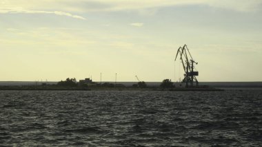 Küçük bir kargo limanındaki vinçler gün batımında çalışmaya başlamak için bekliyorlar..