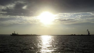 Gün batımında sakin bir denizde sahil kenarındaki yolda çelik bir geminin silueti..