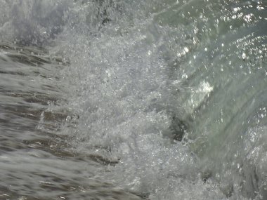 Deniz yeşili dalgalar kumlu kumsalın üzerinde akıyor, kumların üzerinde beyaz bir köpük bırakıyor..