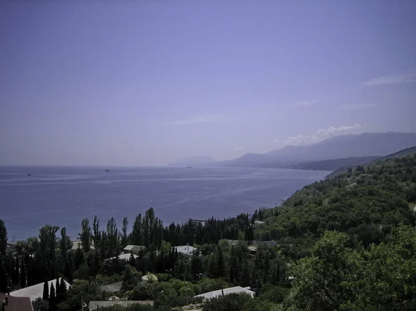 Sea view from the coastal mountains. The coastal hills are surrounded by dense vegetation, including low buildings. In the distance, on the horizon, you can see the coastal mountains in the haze.
