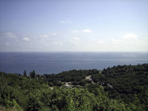 Sea view from the coastal mountains. The coastal hills are surrounded by dense vegetation, including low buildings. In the distance, on the horizon, you can see the coastal mountains in the haze.