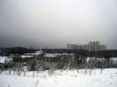 Bulutlu bir havada, kış ormanındaki yüksek bir tepeden yüksek yerleşim alanlarının manzarası..