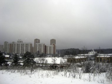 Bulutlu bir havada, kış ormanındaki yüksek bir tepeden yüksek yerleşim alanlarının manzarası..