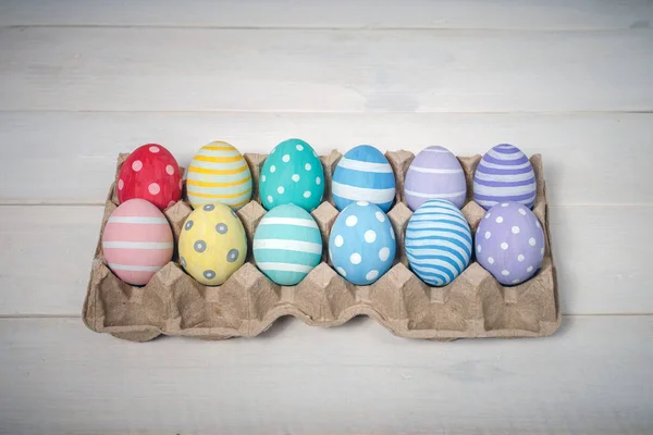 Una bandeja con doce coloridos huevos de Pascua hechos a mano se encuentra sobre fondo de madera blanca, en el centro . — Foto de Stock