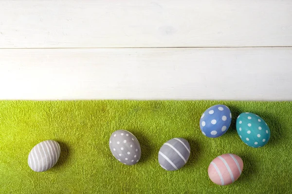 Seis coloridos huevos de Pascua hechos a mano yacen en un césped verde sobre un fondo de madera blanca. Estilo laico plano — Foto de Stock