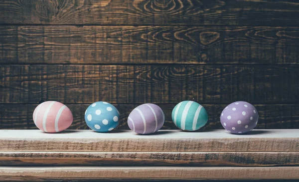 Cinco coloridos huevos de Pascua hechos a mano yacen en una fila sobre una pila de tablas sobre un fondo de madera. Con efecto de filtro retro — Foto de Stock