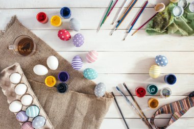 Paskalya için hazırlık. Renkli el yapımı Paskalya yumurtaları boya, fırça üzerinde beyaz ahşap arka plan donatmak. Üstten Görünüm. Düz yatıyordu arpacık