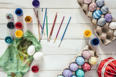 Paskalya için hazırlık. Renkli el yapımı Paskalya yumurtaları boya, fırça üzerinde beyaz ahşap arka plan donatmak. Üstten Görünüm. Düz yatıyordu arpacık