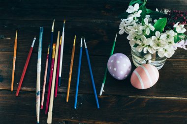 Paskalya için hazırlık. Renkli el yapımı Paskalya yumurtaları, fırçalar ve koyu ahşap arka plan üzerinde çiçekli vazo