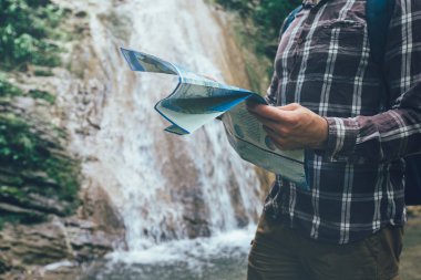Tanınmayan genç seyahat etmek sırt çantası ile şelale tarafından ayakta harita tatil ve Turizm kavramı ele almaktadır