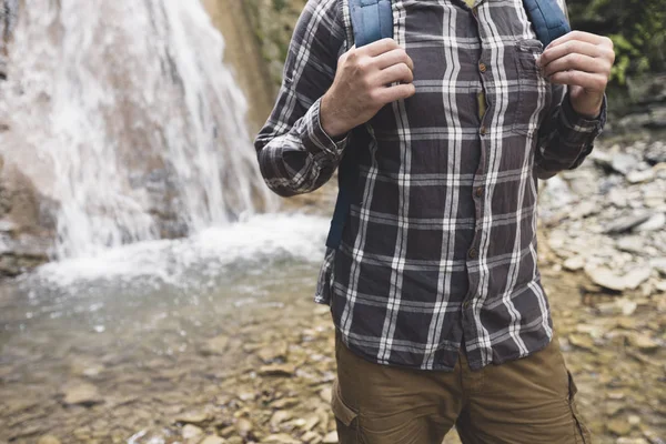 Mãos de caminhante irreconhecíveis mantém a cinta da mochila no fundo da cachoeira Caminhadas conceito de viagem — Fotografia de Stock