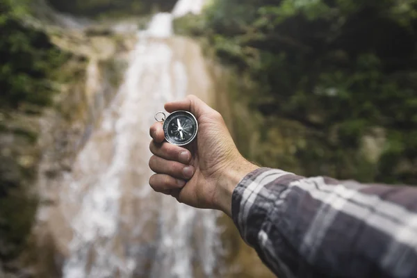 Mannen Explorer söker riktning med kompass på vattenfall bakgrund, synpunkt Fotvandring resa resor Trek koncept — Stockfoto