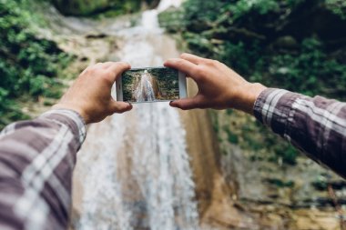 Macera uzun yürüyüşe çıkan kimse adam ayaklar, Backback ve termos şelale arka plan üzerinde