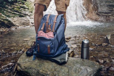 Uzun yürüyüşe çıkan kimse adam ayaklar, sırt çantası ve termos şelale arka plan macera seyahat kavramı Hiking