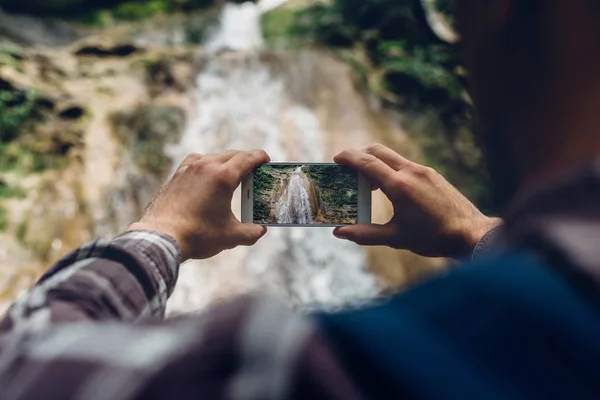 Mãos do viajante tirando foto de cachoeira com suas tecnologias de desenvolvimento de smartphones para o conceito de turismo — Fotografia de Stock