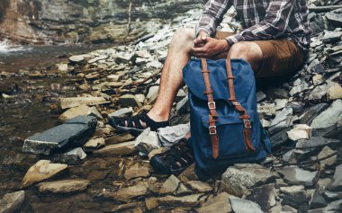 Tanınmayan erkek Hiker Nehri üzerinde oturur ve kavram Hiking macera keşfetmek görünümü çevreleyen sahiptir