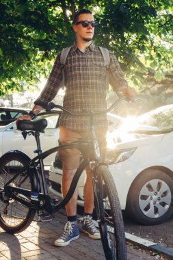 Bisiklet yakınındaki yaz araba günlük rutin yaşam tarzı ile ayakta güneş gözlüklü genç adam