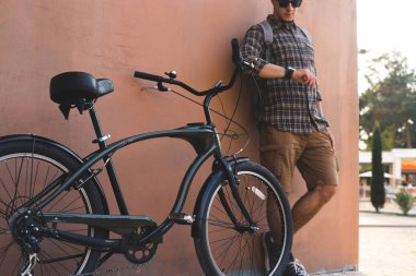 Stand Bisiklet duvar arka plan ve saatine bakar yakınındaki genç adam