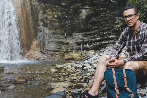 Mochilero macho sentado en las rocas cerca de la cascada Senderismo Destino Experiencia Estilo de vida Concepto — Foto de Stock