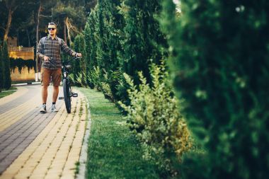 Genç adam Bisikletin üstünde yaz Park tatil hafta sonu etkinliği ile yürüme güneş gözlüğü