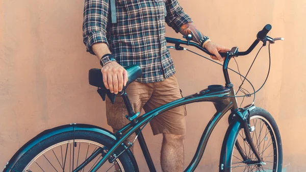 Irreconocible joven hipster hombre sosteniendo las manos en su bicicleta mientras de pie cerca de pared vacaciones actividad concepto — Foto de Stock