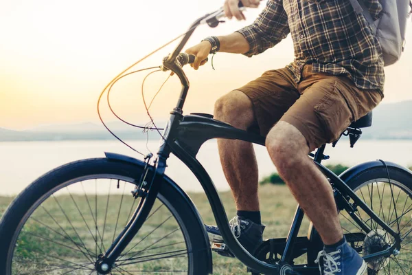 Hombre joven irreconocible está en bicicleta a lo largo de la orilla en el contexto del concepto de actividad de vacaciones al atardecer — Foto de Stock