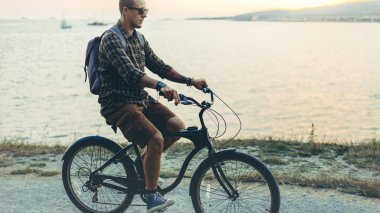 Yakışıklı genç Hipster adam karşı günbatımı tatil tatil etkinlik kavramı zemin ve kıyı Bisiklete binme