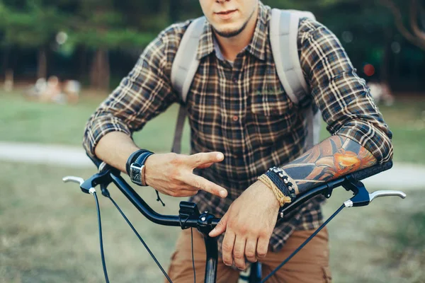 Ung Man visar ett tecken på fred eller seger sitter på en cykel på grön sommaräng — Stockfoto