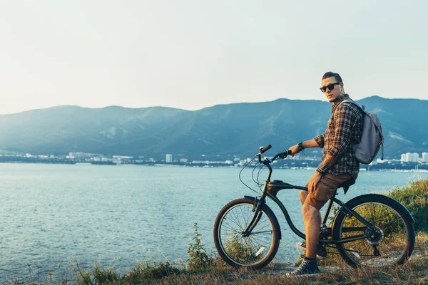 Hombre guapo ciclista de pie con bicicleta en la costa y disfrutando de la vista de la naturaleza Puesta de sol vacaciones viajando Relajación Descanso Destino Concepto — Foto de Stock