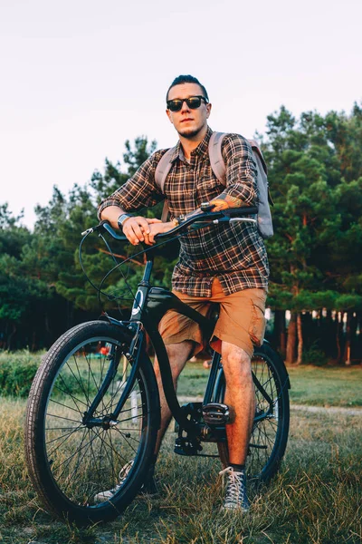 Guapo joven ciclista en gafas de sol con bicicleta en el parque de verano durante las vacaciones al atardecer viajando Relajación Descanso Concepto — Foto de Stock
