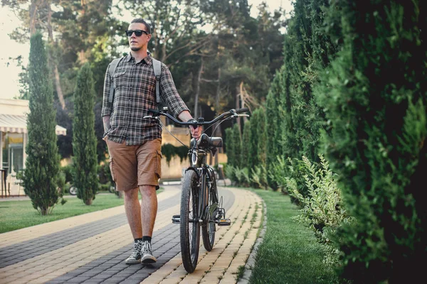 Guapo joven en gafas de sol caminando con bicicleta en verano parque vacaciones actividad concepto — Foto de Stock