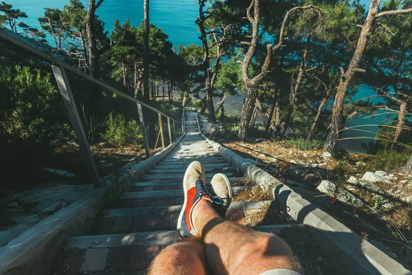 Caminante sentado en las escaleras de la costa sobre el mar, vista de las piernas. Punto de vista Shot — Foto de Stock