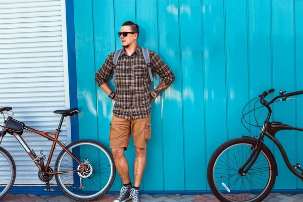 Hombre adulto guapo en gafas de sol se para con una bicicleta a lo largo de una pared azul estilo de vida diario Urban Resting Concept — Foto de Stock