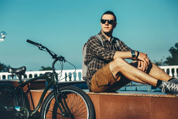 Young Man Cyclist Sitting On Fountain Next To Bicycle In Summer Park Daily Lifestyle Urban Resting Concept — Stock Photo, Image