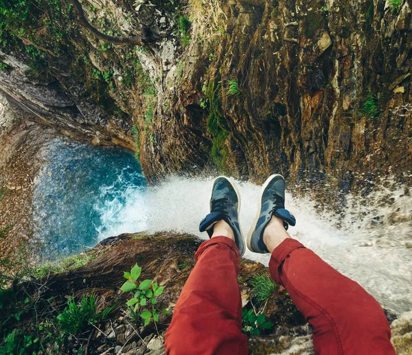 Hombre viajero sentado en el acantilado con vista a la cascada. Viajes Vida aventura vacaciones concepto — Foto de Stock