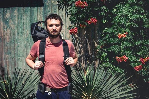 Hombre joven excursionista con mochila de pie cerca de la vieja pared de madera con plantas — Foto de Stock