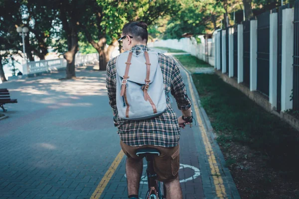 Joven con mochila montando una bicicleta a través del parque de plantas, vista trasera, estilo de vida diario Urban Resting Concept — Foto de Stock